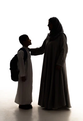 The feeling of safety and love with mothers, the back-to-school season in Saudi Arabia, the concept of caring for and paying attention to children, a silhouette of an Arab Gulf Saudi boy wearing a white thobe and a school bag standing with his mother, preparing for the school year, full-body, white background, silhouette.