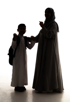 مفهوم الفرح بالنصر والفوز، النجاح وتحقيق الأهداف، موسم العودة للمدارس في السعودية، مفهوم الاعتناء بالأبناء والاهتمام بهم،  صورة ظلية لولد عربي خليجي سعودي يرتدي الثوب الابيض و الحقيبة المدرسية يقف برفقة والدته، الاستعداد للعام الدراسي، الجسم بالطول الكامل، خلفية بيضاء ، سولوليت