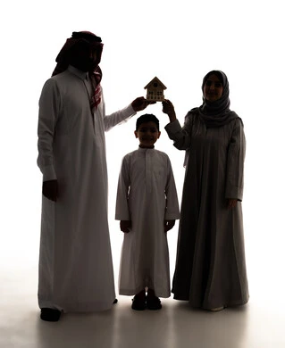الروابط الأسرية القوية، السعي لامتلاك بيت جديد، بيع وشراء العقارات، صورة ظلية لعائلة عربيه خليجيه سعودية ترتدي الزي التقليدي يحملان بيديهم مجسم خشبي صغير لمنزل، إيماءات السرور والسعادة، الجسم بالطول الكامل، خلفية بيضاء ، سولوليت