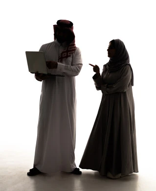 العمل عن بعد، استخدام الأجهزة التقنية الحديثة والمتطورة، ادارة شؤون الاعمال وتنظيمها، امراة سعودية محجبه تشير الى شيء ما، تصفح مواقع التواصل الإجتماعي ،  صورة ظلية لرجل عربي خليجي سعودي  يرتدي  الثوب الابيض و الشماغ يستخدم الحاسوب المحمول،  الجسم بالطول الكامل، خلفية بيضاء، سولوليت