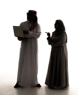 استخدام الأجهزة التقنية الحديثة والمتطورة، ادارة شؤون الاعمال وتنظيمها، العمل عن بعد، امراة سعودية محجبه تشير الى شيء ما، تصفح مواقع التواصل الإجتماعي ،  صورة ظلية لرجل عربي خليجي سعودي  يرتدي  الثوب الابيض و الشماغ يستخدم الحاسوب المحمول،  الجسم بالطول الكامل، خلفية بيضاء، سولوليت