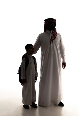 الشعور بالأمان والحب مع الآباء، موسم العودة للمدارس في السعودية، مفهوم الاعتناء بالأبناء والاهتمام بهم، صورة ظلية لولد عربي خليجي سعودي يرتدي الثوب الابيض يضع الحقيبة على ظهره يقف برفقه والده، الاستعداد للعام الدراسي، الجسم بالطول الكامل، خلفية بيضاء ، سولوليت