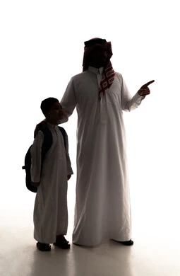الاشارة الى شيء ما، الشعور بالأمان والحب مع الآباء، موسم العودة للمدارس في السعودية، مفهوم الاعتناء بالأبناء والاهتمام بهم، صورة ظلية لولد عربي خليجي سعودي يرتدي الثوب الابيض يضع الحقيبة على ظهره يقف برفقه والده، الاستعداد للعام الدراسي، الجسم بالطول الكامل، خلفية بيضاء ، سولوليت