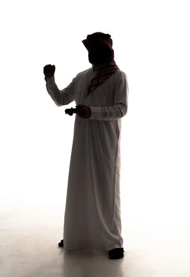 رفع قبضة اليد للاعلى بتعابير الفوز و الربح, اجهزة وتقنيات الكترونية حديثة ترفيهيه, قضاء وقت ممتع ومسلي، التفاعل والاندماج مع ألعاب الفيديو والبلايستيشن،, صورة ظلية لرجل عربي خليجي سعودي يرتدي الثوب الابيض و الشماغ يحمل بيده عصا التحكم، الجسم بالطول الكامل، خلفية بيضاء، سولوليت