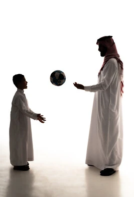 مشاركة الأبناء لحظات مرحة ، مفهوم اللياقة والرشاقة البدنية، الاستمتاع بممارسة الأنشطة والرياضات الشبابية،صورة ظلية لرجل عربي خليجي سعودي يرتدي الثوب الابيض و الشماغ يقوم بلعب كرة القدم مع ابنه ، قضاء اوقت ممتعة،الجسم بالطول الكامل، خلفية بيضاء ، سولوليت