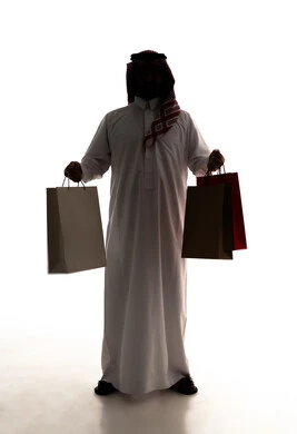 Promoting global products and brands, buying necessities and gifts, taking advantage of offers and discounts, the joy of shopping in commercial malls, a silhouette of an Arab Gulf Saudi man wearing a white thobe and a ghutrah holding a paper bag in his hands, full-body, white background, silhouette.
