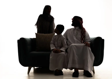 مفهوم الحب و الترابط الاسري، صورة ظلية لعائلة عربية خليجيه سعودية ترتدي الزي التقليدي يجلسون على الاريكة ينظرون الى بعض بايماءات السعادة و السرور، قضاء أوقات عائلية ممتعة، خلفية بيضاء ، سولوليت