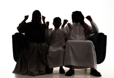 تحقيق النجاح والانتصار في المنافسات، صورة ظلية لعائلة عربيه خليجيه سعودية ترتدي الزي التقليدي يجلسون على الاريكه يقومون برفع ايديهم للاعلي بايماءات السرور والسعاده، مفهوم الفوز بالبطولات، خلفية بيضاء ، سولوليت