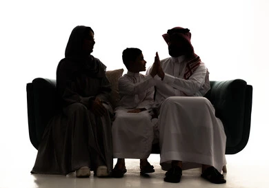 The concept of love and affection between children, gestures of high-fiving, spending enjoyable time playing with the kids, a silhouette of an Arab Gulf Saudi father wearing a white thobe and a ghutrah sitting on a couch with his wife, pointing with his hand opposite his son's hand, white background, silhouette.