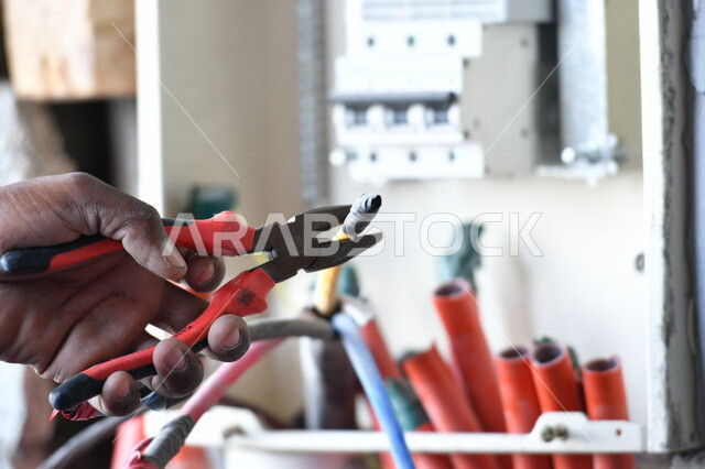 Close-up picture of the hand of an Arab Saudi Arabian Gulf electrical engineer, cutting electrical wires using pliers, electrical tools, electrical engineering