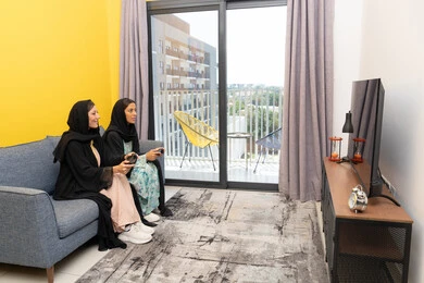 Excitement, interaction and integration into the modern and advanced digital electronic world, enjoyable and entertaining entertainment experiences, participation in video games, two Saudi women holding the joystick with concentration, two Arab Gulf Emirati women competing to achieve victory and triumph