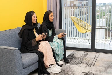 تجارب ترفيهية ممتعة ومسلية, المشاركة بألعاب الفيديو جيمز, إمرأتان سعوديتان تمسكان عصا التحكم بتركيز, سيدتان عربيتان خليجيتان إماراتيتان تتنافسان لتحقيق الفوز والانتصار، الحماس والتفاعل والاندماج بالعالم الرقمي الالكتروني الحديث والمتطور