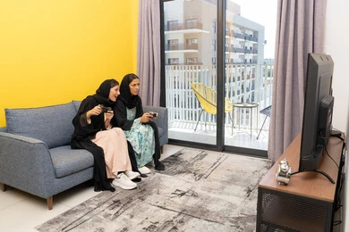 Interaction, enthusiasm and integration into the modern and advanced digital electronic world, enjoyable and entertaining entertainment experiences, participation in video games, two Saudi women holding the joystick with concentration, two Arab Gulf Emirati women competing to achieve victory and triumph