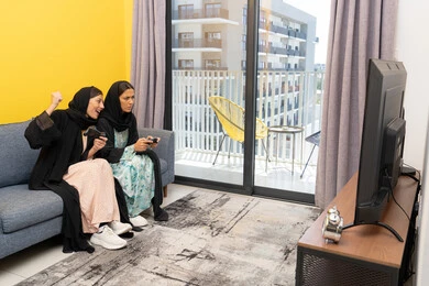 Fun and entertaining entertainment experiences, participating in video games, two Saudi women holding the joystick with concentration, two Arab Gulf Emirati women competing to achieve victory and triumph, enthusiasm, interaction and integration into the modern and advanced electronic digital world