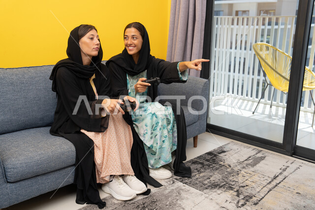 المشاركة بألعاب الفيديو جيمز, إمرأتان سعوديتان تمسكان عصا التحكم بتركيز, سيدتان عربيتان خليجيتان إماراتيتان تتنافسان لتحقيق الفوز والانتصار، الحماس والتفاعل والاندماج بالعالم الرقمي الالكتروني الحديث والمتطور، تجارب ترفيهية ممتعة ومسلية