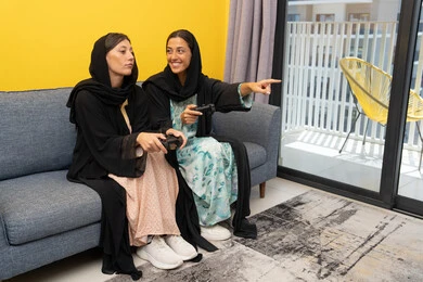 Participating in video games, two Saudi women holding a joystick with concentration, two Arab Gulf Emirati women competing to achieve victory, enthusiasm, interaction and integration into the modern and advanced electronic digital world, enjoyable and entertaining entertainment experiences Participating in video games, two Saudi women holding a joystick with concentration, two Arab Gulf Emirati women competing to achieve victory, enthusiasm, interaction and integration into the modern and advanced electronic digital world, enjoyable and entertaining entertainment experiences