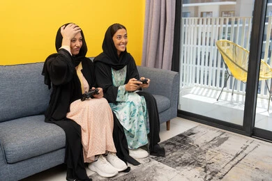 Excitement, interaction and integration into the modern and advanced digital electronic world, enjoyable and entertaining entertainment experiences, participation in video games, two Saudi women holding the joystick with concentration, two Arab Gulf Emirati women competing to achieve victory and triumph