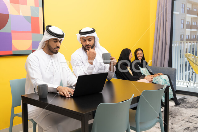 إمرأتان ترتديان العباءة والحجاب تتبادلان الاحاديث، إدارة شؤون الأعمال وتنظيمها عبر اللابتوب، الاستمتاع بالجلوس في المنزل، استخدام جهاز تقني حديث ومتطور، رجلان عربيان خليجيان اماراتيان يرتديان الكندورة والغترة يعملان على الحاسوب المحمول، إنجاز مهام العمل عن بعد