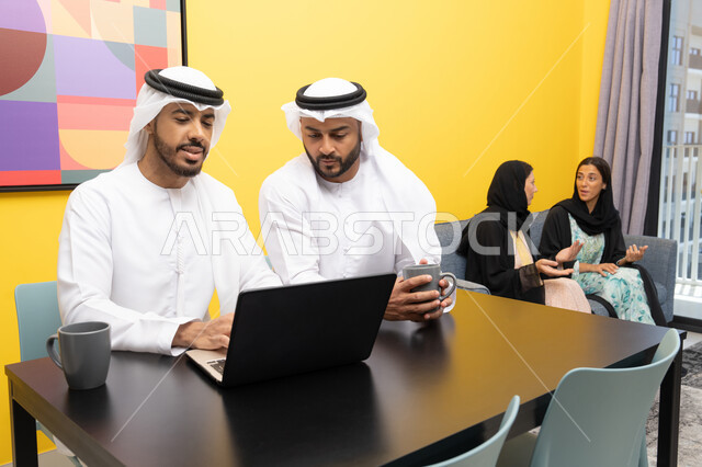 إمرأتان ترتديان العباءة والحجاب تتبادلان الاحاديث، إدارة شؤون الأعمال وتنظيمها عبر اللابتوب، الاستمتاع بالجلوس في المنزل، استخدام جهاز تقني حديث ومتطور، رجلان عربيان خليجيان اماراتيان يرتديان الكندورة والغترة يعملان على الحاسوب المحمول، إنجاز مهام العمل عن بعد