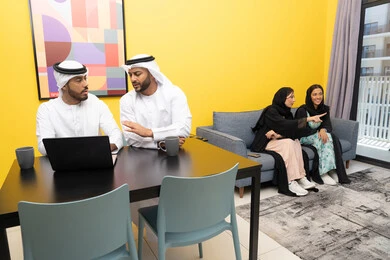 إنجاز مهام العمل عن بعد، إمرأتان ترتديان العباءة والحجاب تتبادلان الاحاديث، إدارة شؤون الأعمال وتنظيمها عبر اللابتوب، الاستمتاع بالجلوس في المنزل، استخدام جهاز تقني حديث ومتطور، رجلان عربيان خليجيان اماراتيان يرتديان الكندورة والغترة يعملان على الحاسوب المحمول