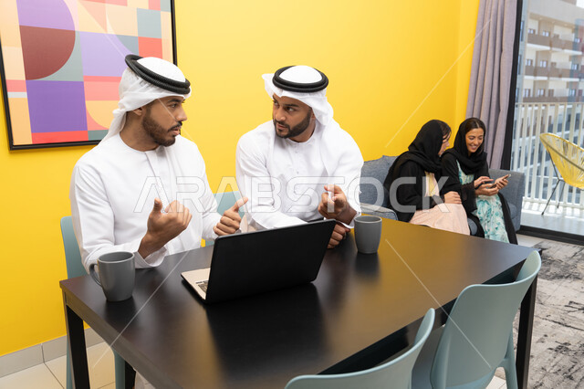 إمرأتان ترتديان العباءة والحجاب تتبادلان الاحاديث، إدارة شؤون الأعمال وتنظيمها عبر اللابتوب، الاستمتاع بالجلوس في المنزل، استخدام جهاز تقني حديث ومتطور، رجلان عربيان خليجيان اماراتيان يرتديان الكندورة والغترة يعملان على الحاسوب المحمول، إنجاز مهام العمل عن بعد