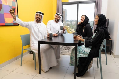 توثيق اللحظات السعيدة، التقاط صور التذكارية عبر الجوال، اصدقاء عرب خليجيون اماراتيون يرتدون الزي التقليدي يقومون بالتجمع على الطاولة فى المنزل، مفهوم التقنيات والأجهزة الحديثة، تطوير العلاقات الإجتماعية، ايماءات السعادة والسرور، قضاء وقت ممتع برفقة الأصدقاء