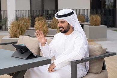 اجراء مكالمه فيديو، استخدم جهاز التابلت لانجاز المشاريع والمهام ،الاستمتاع بالمشروبات الساخنه ، مفهوم التكنولوجيا وإستخدام تقنيات حديثة، قضاء وقت ممتع فى الخارج ،شاب عربي خليجي إماراتي يرتدي الكندورة والغترة البيضاء يجلس في المقهى