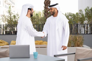 صداقات وتعارف ونقاشات وحوارات ،اعياد ومناسبات سعيدة ، رجلان عربيان خليجيان اماراتيان يرتديان الكندورة والغتره يتصافحان بحرارة،عادات العيد في المجتمع الاماراتي ،قضاء أوقات ممتعة مع الاصدقاء ، كوفي شوب راقي