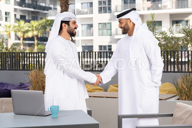اعياد ومناسبات سعيدة ، رجلان عربيان خليجيان اماراتيان يرتديان الكندورة والغتره يتصافحان بحرارة،عادات العيد في المجتمع الاماراتي ،قضاء أوقات ممتعة مع الاصدقاء ، كوفي شوب راقي ،صداقات وتعارف ونقاشات وحوارات