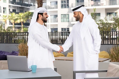 اعياد ومناسبات سعيدة ، رجلان عربيان خليجيان اماراتيان يرتديان الكندورة والغتره يتصافحان بحرارة،عادات العيد في المجتمع الاماراتي ،قضاء أوقات ممتعة مع الاصدقاء ، كوفي شوب راقي ،صداقات وتعارف ونقاشات وحوارات