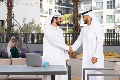 رجلان عربيان خليجيان اماراتيان يرتديان الكندورة والغتره يتصافحان بحرارة،عادات العيد في المجتمع الاماراتي ،قضاء أوقات ممتعة مع الاصدقاء ، كوفي شوب راقي ،صداقات وتعارف ونقاشات وحوارات ، اعياد ومناسبات سعيدة