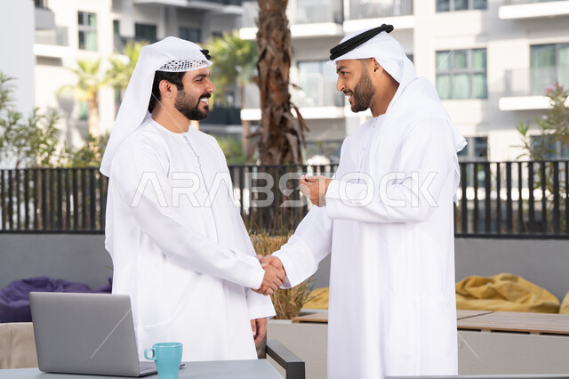 كوفي شوب راقي ، قضاء أوقات ممتعة مع الاصدقاء ، صداقات وتعارف ونقاشات وحوارات ، عادات العيد في المجتمع الاماراتي ، رجلان عربيان خليجيان اماراتيان يرتديان الكندورة والغتره يتصافحان بحرارة، اعياد ومناسبات سعيدة