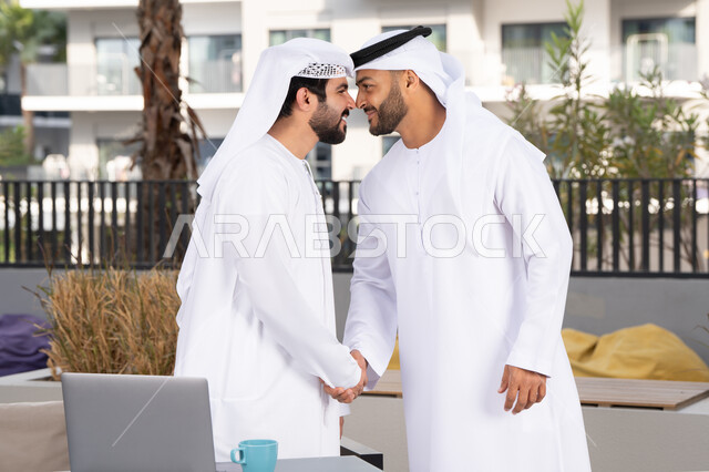 Spending quality time with friends, friendships, acquaintances, discussions, and dialogues, Eid customs in Emirati society, two Emirati Gulf Arab men wearing kandoras and ghutras, shaking hands warmly, happy holidays and occasions, a classy coffee shop