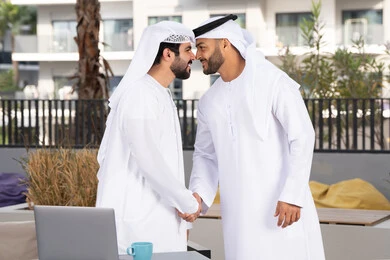 قضاء أوقات ممتعة مع الاصدقاء ، صداقات وتعارف ونقاشات وحوارات ، عادات العيد في المجتمع الاماراتي ، رجلان عربيان خليجيان اماراتيان يرتديان الكندورة والغتره يتصافحان بحرارة، اعياد ومناسبات سعيدة ،كوفي شوب راقي