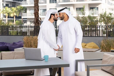 صداقات وتعارف ونقاشات وحوارات ، عادات العيد في المجتمع الاماراتي ، قضاء أوقات ممتعة مع الاصدقاء ، رجلان عربيان خليجيان اماراتيان يرتديان الكندورة والغتره يتصافحان بحرارة، اعياد ومناسبات سعيدة ،كوفي شوب راقي