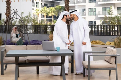 عادات العيد في المجتمع الاماراتي ، صداقات وتعارف ونقاشات وحوارات ، قضاء أوقات ممتعة مع الاصدقاء ، رجلان عربيان خليجيان اماراتيان يرتديان الكندورة والغتره يتصافحان بحرارة، اعياد ومناسبات سعيدة ،كوفي شوب راقي