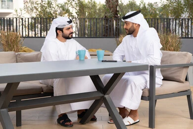 A classy coffee shop in the Emirates, spending a pleasant time with friends, enjoying the happy atmosphere, two Emirati Gulf Arab friends wearing the white kandura and ghutra, exchanging conversation with expressions of pleasure
