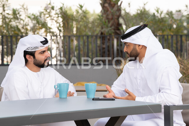 قضاء اوقات ممتعه مع الاصدقاء ، الاستمتاع بالاجواء السعيده ، كوفي شوب راقي بالامارات ، صديقان عربيان خليجيان اماراتيان يرتديان الكندورة والغترة البيضاء، يتبادلان الحديث بتعابير السرور