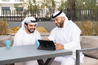 ايماءات الاندماج والتركيز ، الحوار والنقاش بين زملاء العمل، شاب عربي خليجي إماراتي يرتدي الكندورة والغترة البيضاء يجلس مع صديقه في المقهى ، الاستمتاع بالمشروبات الساخنه، استخدم جهاز التابلت لانجاز المشاريع والمهام في الكافيه، قضاء وقت ممتع مع الأصدقاء