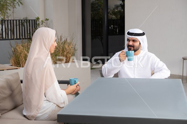 قضاء أوقات ممتعة ورومانسية، زوجان عربيان خليجيان اماراتيان مبتسمان يجلسان في المقهى ، مفهوم المودة والالفة ، ايماءات السرور والسعادة ،الاستمتاع بشرب المشروبات الساخنه