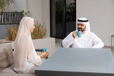 قضاء أوقات ممتعة ورومانسية، زوجان عربيان خليجيان اماراتيان مبتسمان يجلسان في المقهى ، مفهوم المودة والالفة ، ايماءات السرور والسعادة ،الاستمتاع بشرب المشروبات الساخنه