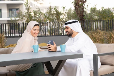 ايماءات السرور والسعادة ، قضاء شهر العسل، الاستمتاع بشرب المشروبات الساخنه ، رجل عربي يقوم بإلتقاط صورة سيلفي تذكارية له و لزوجته ، مفهوم المودة والالفة ، قضاء أوقات ممتعة، زوجان عربيان خليجيان اماراتيان مبتسمان يجلسان في المقهى