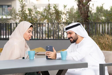 الاستمتاع بشرب المشروبات الساخنه ، رجل عربي يقوم بإلتقاط صورة سيلفي تذكارية له و لزوجته ،  ايماءات السرور والسعادة ، مفهوم المودة والالفة ، قضاء أوقات ممتعة، زوجان عربيان خليجيان اماراتيان مبتسمان يجلسان في المقهى ، قضاء شهر العسل