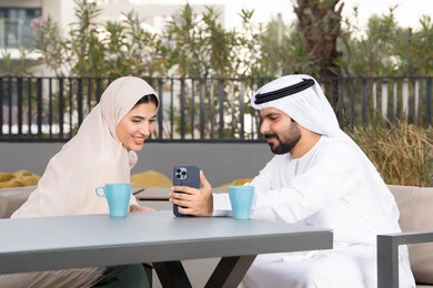 ايماءات السرور والسعادة ، قضاء شهر العسل، الاستمتاع بشرب المشروبات الساخنه ، رجل عربي يقوم بإلتقاط صورة سيلفي تذكارية له و لزوجته ، مفهوم المودة والالفة ، قضاء أوقات ممتعة، زوجان عربيان خليجيان اماراتيان مبتسمان يجلسان في المقهى