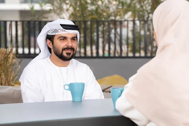 قضاء أوقات ممتعة ورومانسية، زوجان عربيان خليجيان اماراتيان مبتسمان يجلسان في المقهى ، مفهوم المودة والالفة ، ايماءات السرور والسعادة ،الاستمتاع بشرب المشروبات الساخنه