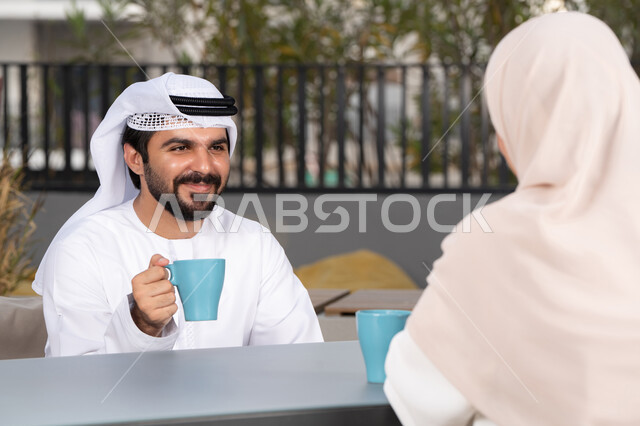 زوجان عربيان خليجيان اماراتيان مبتسمان يجلسان في المقهى ، مفهوم المودة والالفة ، ايماءات السرور والسعادة ،الاستمتاع بشرب المشروبات الساخنه ،  قضاء أوقات ممتعة ورومانسية
