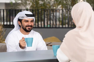 Smiling Emirati Gulf Arab couple sitting in a cafe, the concept of affection and intimacy, gestures of pleasure and happiness, enjoying drinking hot drinks, spending fun and romantic times