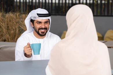 مفهوم المودة والالفة ، ايماءات السرور والسعادة ،الاستمتاع بشرب المشروبات الساخنه ،  قضاء أوقات ممتعة ورومانسية،زوجان عربيان خليجيان اماراتيان مبتسمان يجلسان في المقهى