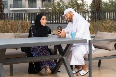 رجل عربي يقوم بإلتقاط صورة سيلفي تذكارية له و لزوجته ،  ايماءات السرور والسعادة ، مفهوم المودة والالفة ، قضاء أوقات ممتعة، زوجان عربيان خليجيان اماراتيان مبتسمان يجلسان في المقهى ، يستمتعان بشرب القهوة الساخنة ، الاستمتاع بالاجواء العائلية ، قضاء شهر العسل