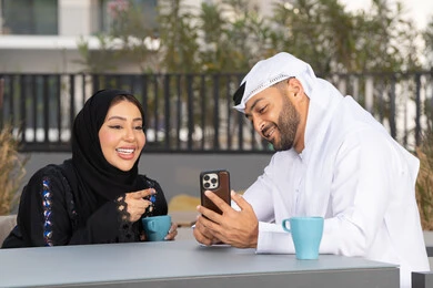 ايماءات السرور والسعادة ، مفهوم المودة والالفة ، قضاء أوقات ممتعة، زوجان عربيان خليجيان اماراتيان مبتسمان يجلسان في المقهى ، يستمتعان بشرب القهوة الساخنة ، رجل عربي يقوم بإلتقاط صورة سيلفي تذكارية له و لزوجته ، الاستمتاع بالاجواء العائلية ، قضاء شهر العسل